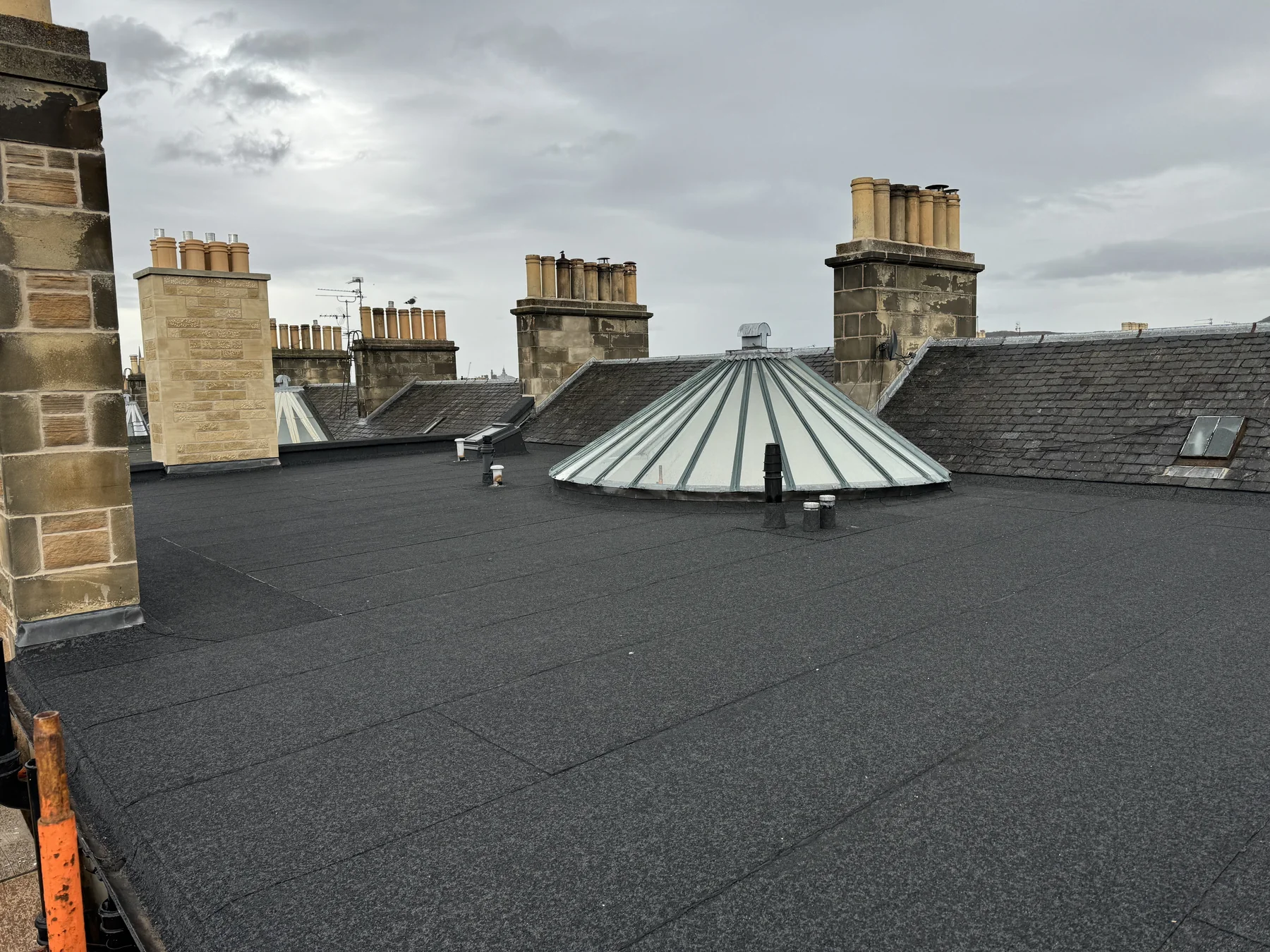 Felt flat roof with glazed cupola surrounded by tenement chimney stacks at Arden Street, Edinburgh