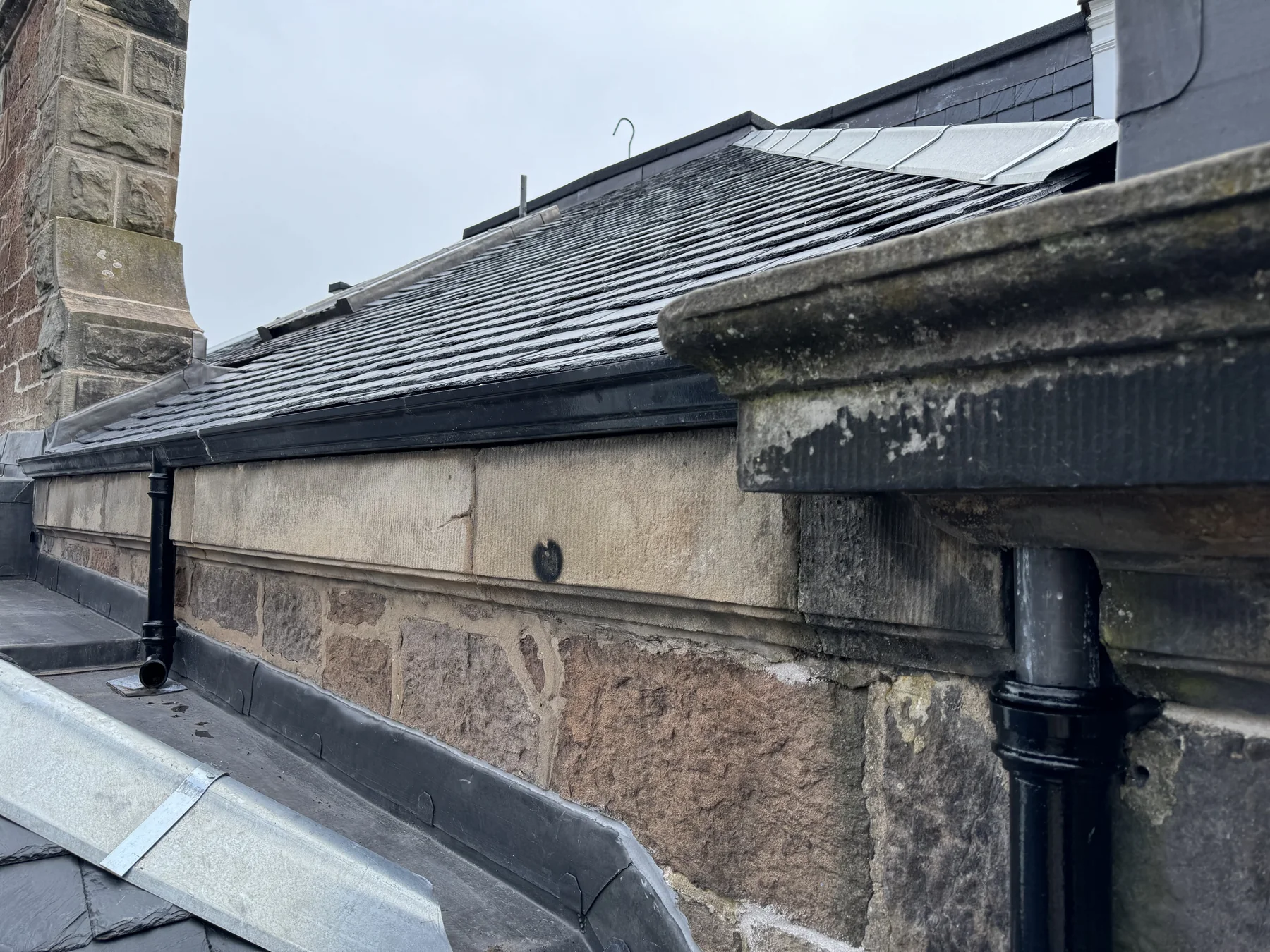Black rainwater downpipes and gutters fitted to sandstone eaves below a slate roof at Cromwell Road, Edinburgh